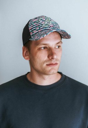 Cap features a colorful flamingo and floral pattern with a black mesh back; curved brim; logo accent on the front; adjustable fit.