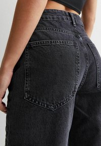 Mustat korkeavyötäröiset farkut, joissa on kaksinkertaiset takataskut, kontrastivärinen saumaus ja suora lahkeiden muoto.