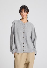 Cardigan lavorato a maglia grigio chiaro con colletto rotondo, sette bottoni sul davanti e polsini e orlo a costine, abbinato a pantaloni beige.