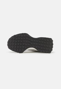 Semelle de chaussure en caoutchouc noir avec des motifs de bande de roulement circulaires, présentant une légère courbe et un bord lisse. Agrémentée d'une section supérieure gris clair.