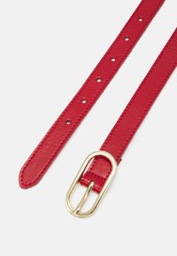 Ceinture en cuir rouge au toucher lisse, ornée d'une boucle ovale dorée et de plusieurs trous pour les ajustements. Les extrémités sont effilées.