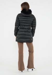 Giacca puffo nera con cappuccio in pelliccia sintetica, design trapuntato e silhouette aderente. Abbinata a pantaloni a zampa d'elefante marroni e sneakers bianche.
