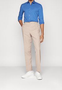 Pantaloni beige chiari abbinati a una camicia azzurra brillante con bottoni e sneakers bianche. La camicia ha maniche lunghe e i pantaloni sono a gamba dritta.