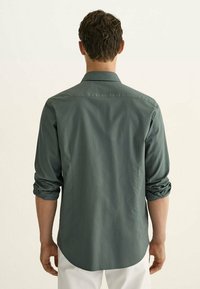 Groen, langemouwen shirt van lichtgewicht stof met een afgeronde zoom en opgerolde manchetten, met een standaard kraag en een gladde textuur.