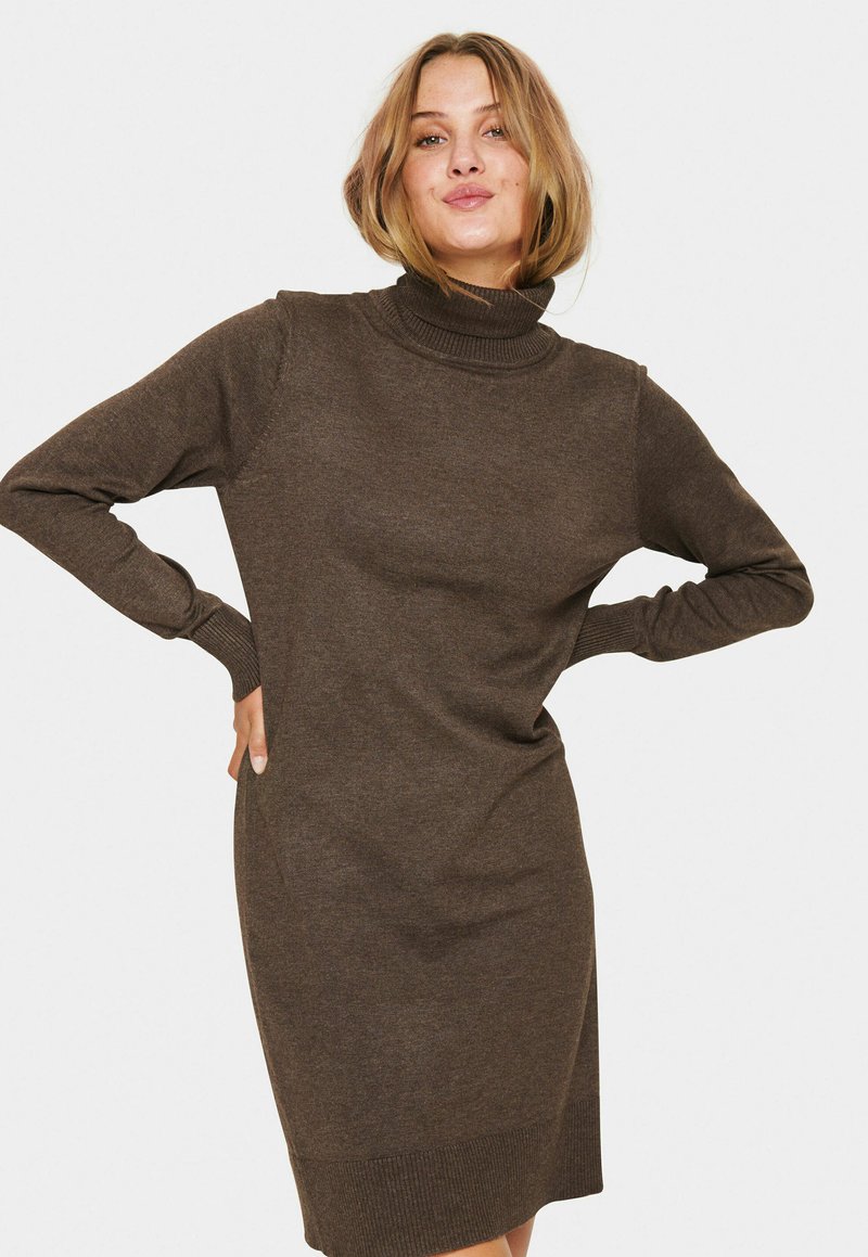 Ruda megzta turtlenecko suknelė su ilgomis rankovėmis, prigludusio silueto, su raukiniais ant rankogalių ir apačios, minkšta tekstūra ir vidutinio ilgio kirpimas.