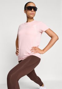 Lys rosa kortermet treningstopp kombinert med brune leggings. antrekket har en jevn tekstur og et tettsittende design for komfort.