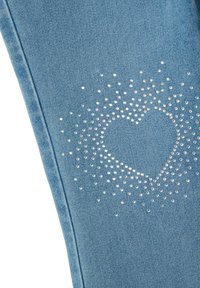 Jeans de mezclilla azul claro con un diseño de corazón brillante hecho de rhinestones multicolores, dispuestos en un patrón degradado.