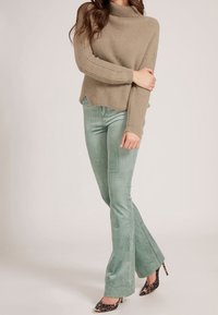 Pull à col roulé en maille côtelée beige, associé à un pantalon évasé en velours côtelé vert clair, et des talons imprimés animal noir et marron.