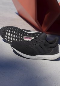 Μαύρα αθλητικά παπούτσια με υφή στην επάνω πλευρά, τριπλή ρίγα και λευκή σόλα. Διαθέτουν μοτίβο στην καουτσούκ σόλα για πρόσφυση.