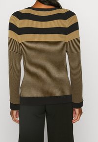 Pull en tricot présentant des rayures horizontales noires et beige, une texture côtelée, un col rond et des poignets noirs. Le design offre une silhouette ajustée.