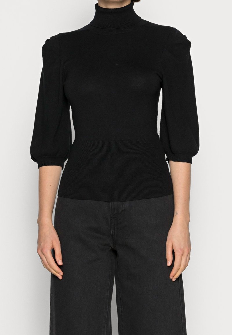 Mannequin féminin portant un pull col roulé noir ajusté avec des manches trois-quarts bouffantes et un pantalon noir taille haute.