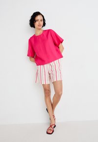 Fuchsia short-sleeve top paired with white shorts featuring red vertical stripes. Model wears black and red flat sandals.