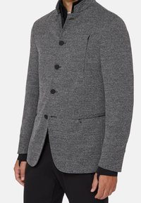 Gray textured jacket featuring a high collar, five black buttons, and side pockets. Material appears wool-like with a herringbone pattern.