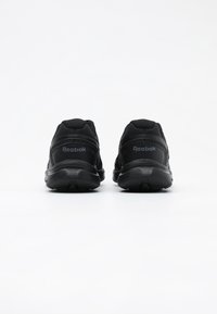 Chaussures de sport noires avec une tige synthétique texturée, une semelle en caoutchouc, un col rembourré et un marquage discret au talon. Design minimaliste.