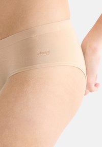 Sous-vêtements beiges sans couture avec une texture lisse et une large ceinture arborant un logo discret. Le tissu semble doux et ajusté au corps.