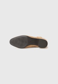 Chaussure en suède beige avec un bout arrondi, semelle en caoutchouc et motif de semelle détaillé. Comprend une boucle sur le côté et un talon lisse.