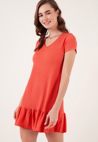 Red, short-sleeved dress with a V-neck and textured fabric, featuring a ruffled hemline and a relaxed fit.