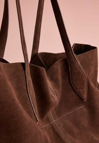 Brown suede tote bag with long handles, soft texture, and stitched accents. Features a spacious interior and a minimalist design.