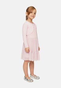 Helles pinkes Kleid mit einem strukturierten Oberteil, mehrlagigem Rock und langen Ärmeln. Kombiniert mit silbernen Flachschuhen mit floralem Akzent.