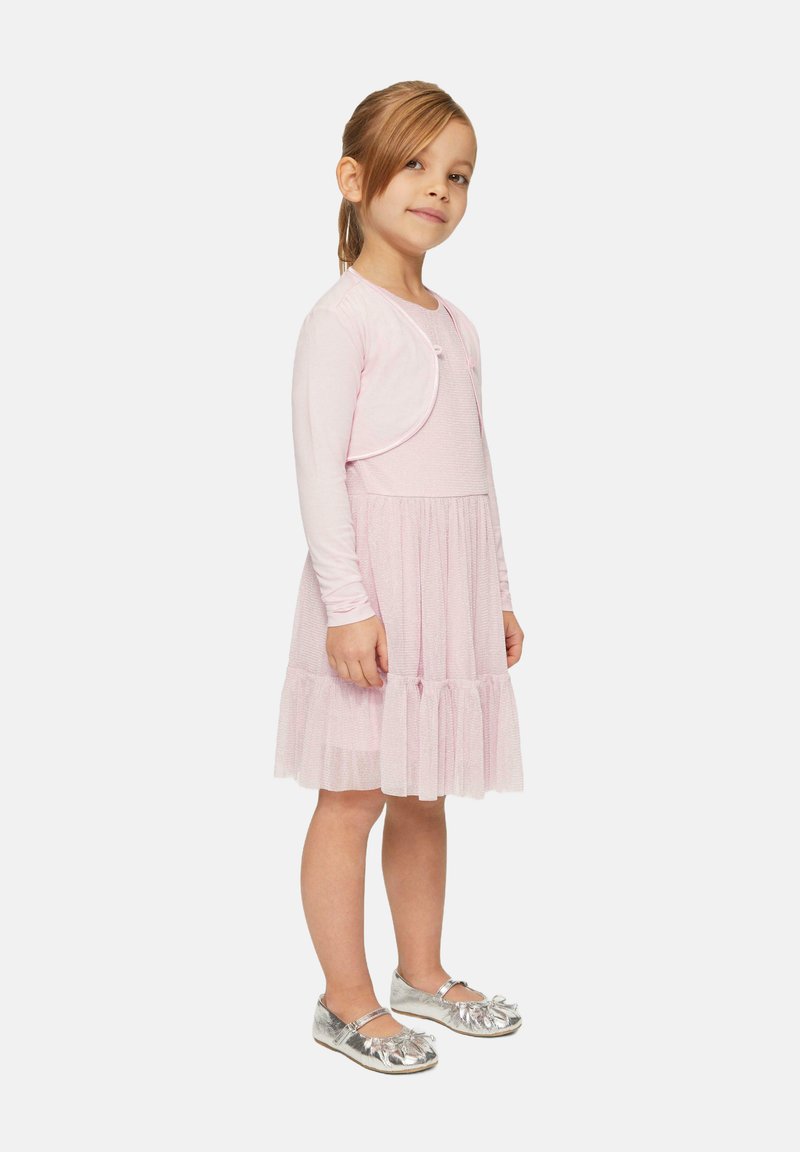 Helles pinkes Kleid mit einem strukturierten Oberteil, mehrlagigem Rock und langen Ärmeln. Kombiniert mit silbernen Flachschuhen mit floralem Akzent.