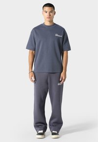 Szara bawełniana koszulka z krótkim rękawem i detalem logo, w połączeniu z dopasowanymi spodniami dresowymi z akcentem logo, noszone z czarnymi sneakersami.