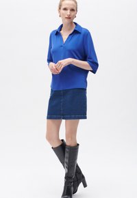 Blå polo skjorta med krage, tillsammans med en mörk denimkjol. Svarta knähöga stövlar med klack fulländar outfiten.