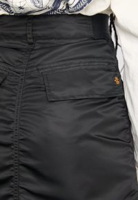 Black padded pants with a smooth texture, featuring a straight waistband, two back pockets, and a small orange logo on the right pocket.