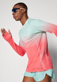 Sportlongsleeve shirt in een verloop van mintgroen naar koraal met fijne horizontale strepen en duimgaten. Draagt in combinatie met bijpassende lichtblauwe shorts.