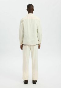 Completo giacca e pantaloni color crema, con una vestibilità rilassata, dettagli di cucitura visibili e design snodato. Tessuto testurizzato con una finitura morbida.