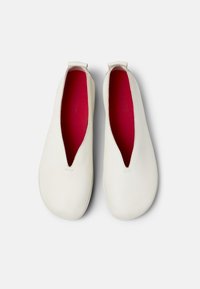 Zapatos blancos de piel de tipo slip-on con un diseño en forma de V y forro interior rosa. Textura suave con detalles de costura mínimos. Suelas planas.