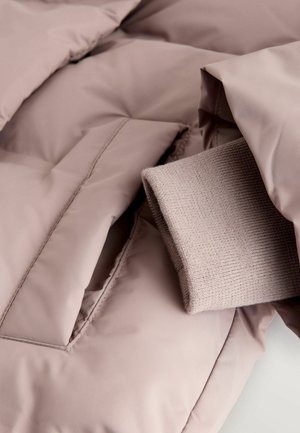 Veste à pince en tissu rose doux, avec une manchette en tricot côtelé à l'intérieur d'une poche. Texture lisse avec des détails cousus.