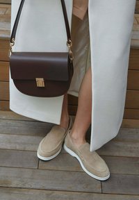 Beige suede slip-on shoes with white soles, paired with a brown leather handbag featuring a gold clasp and a crossbody strap.