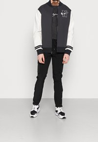 Svart och vit bomberjacka med en solid mörkgrå kropp och vita ärmar, kombinerad med svarta cargobyxor och svart-vita sneakers.