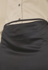 Jupe noire à la texture lisse semblable au satin, avec une fine ceinture, associée à une chemise beige boutonnée en tissu doux.