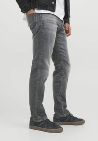 Jeans gri din denim cu o croială slim, având detalii de cusătură subtile și o textura netedă. Purtați cu adidași negri, de tip low-top.
