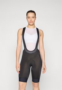 Svart sykkelshorts med nettstropper, en tettsittende design og polstret seteområde. Har en kontrasterende marineblå kant nederst på shortsen.