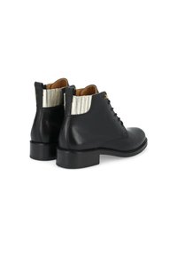 Bottines en cuir noir avec un bout arrondi, un panneau élastique décoratif accentué de argent et un petit talon carrément. Laçage et fermeture zippée sur le côté.