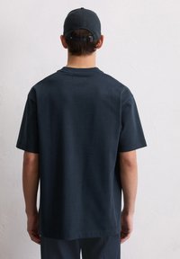 Dunkelblauses Kurzarm-T-Shirt aus Baumwolle mit Rundhalsausschnitt und subtiler Textur, kombiniert mit einer passenden Mütze.