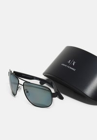 Ochelari de soare metalici negri cu lentile polarizate gri, având o formă aerodinamică și pernițe nazale ajustabile, împreună cu un etui negru cu logo.