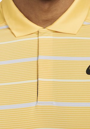 Zbliżenie na żółto-białą koszulkę polo w paski z kołnierzykiem i czarnym logo Nike po prawej stronie.