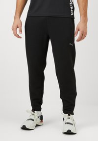 Zwarte sportbroek van textuurstof, met zijzakken, taps toelopende pijpen en een subtiele logo-accent op de linkerdij.