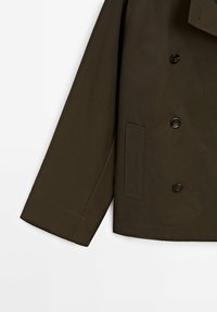 Manche de veste marron foncé et partie inférieure avant avec trois boutons noirs et une poche rectangulaire sur fond blanc.