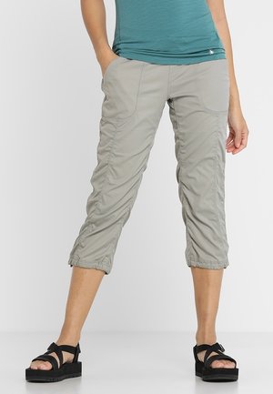 Personne portant un pantalon court gris clair avec des ourlets élastiques, un haut turquoise et des sandales à plateforme noires, se tenant sur un fond uni.