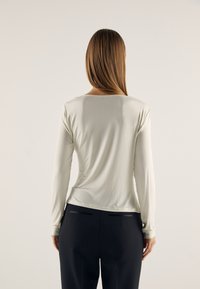 Long-sleeve, light gray top in soft fabric with a scoop neck, paired with dark trousers featuring two back pocket accents.