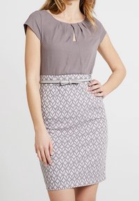 Kortærmet kjole med grå top og mønstret grå nederdel med geometrisk design. Inkluderer et matchende bælte i taljen.
