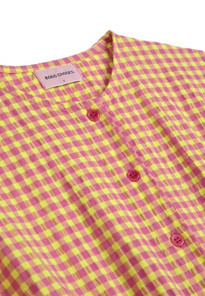 Camisa de cuadros rosa y amarilla hecha de una tela ligera, con un cuello redondo, dos botones rosas y una etiqueta de marca en el cuello.