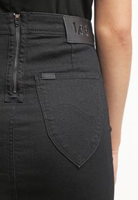 Jeans de mezclilla negra con una cintura alta, con cierre de cremallera, dos bolsillos traseros y un parche de logo de cuero texturizado.