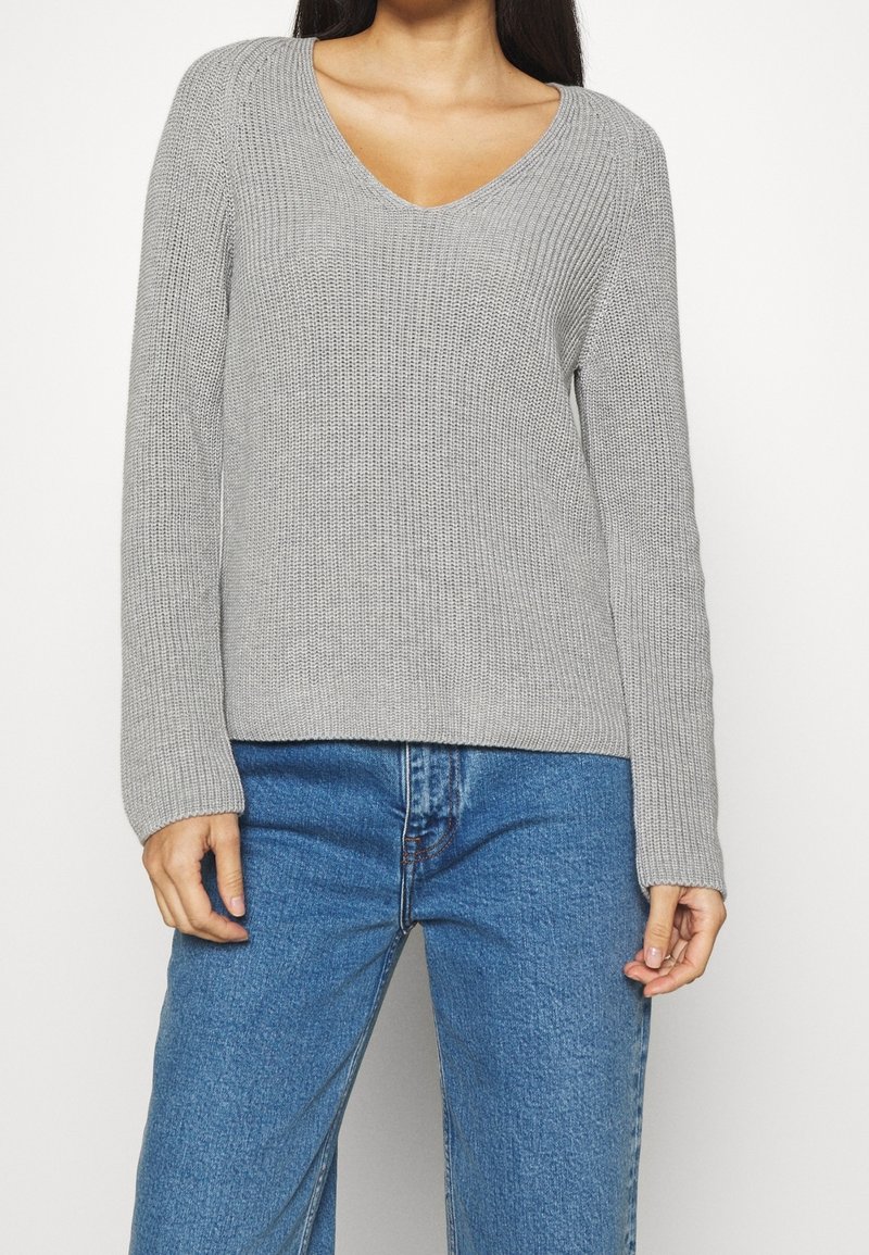 Pull en tricot gris avec un col en V, des manches longues et une texture côtelée, associé à un jean en denim bleu. Coupe décontractée et tissu de poids moyen.