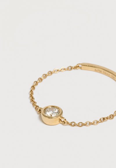 Bracelet délicat en chaîne d’or avec une gemme claire ronde unique sertie dans un chaton en or sur un fond neutre.