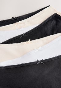 Pięć bawełnianych damskich majtek w kolorach czarnym, białym i beżowym z małymi kokardkami i koronkową lamówką, ułożonych na przemian ukośnie na neutralnym tle.